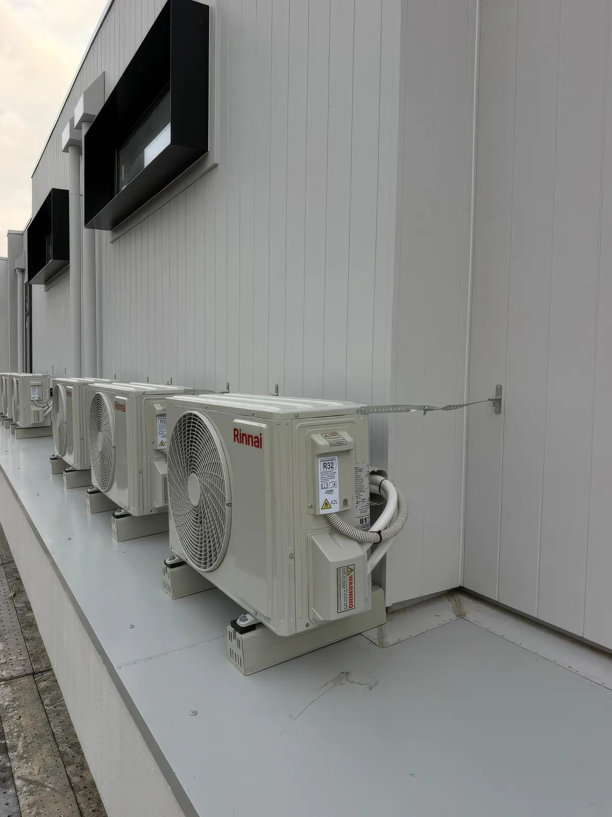 Row of Rinnai condensers on cantilever brackets along a white commercial service wall in Richmond