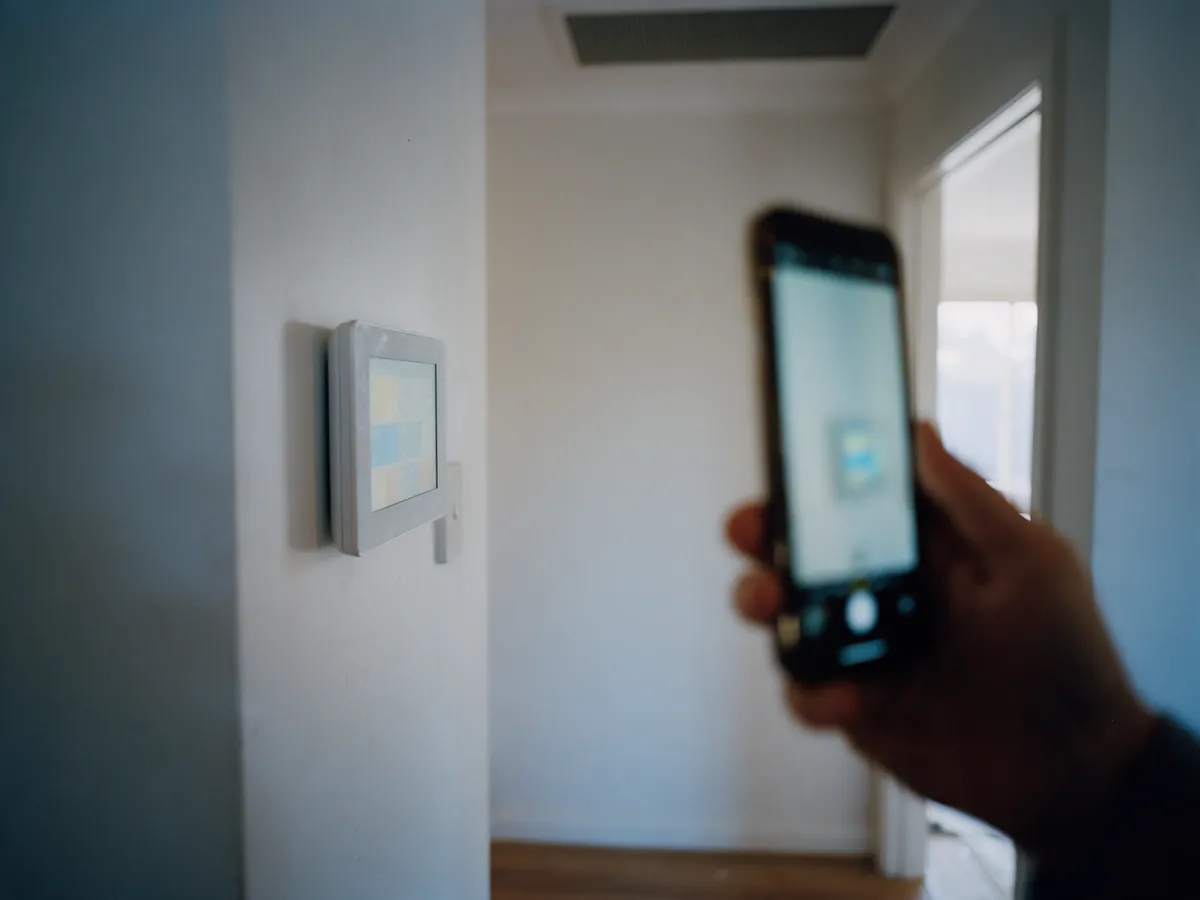 Wall touchscreen climate controller in a hallway with a phone held nearby
