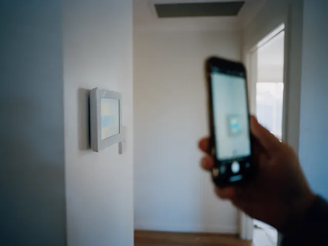 Wall touchscreen climate controller in a hallway with a phone held nearby